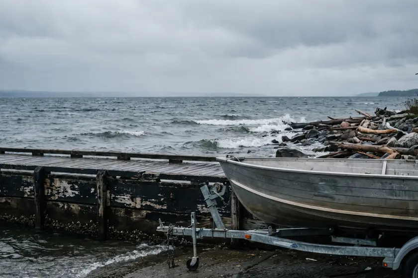 An aluminium fishing boat on a trailer beside a dock on a grey lakeshore
